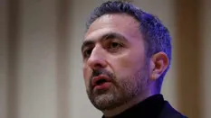Close-up portrait of a man speaking at an event with a serious expression.